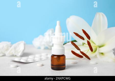 Nasentropfen mit Pillen, Blüten und Taschentüchern auf dem Tisch nahe der blauen Wand, Nahaufnahme. Saisonales Allergiekonzept Stockfoto