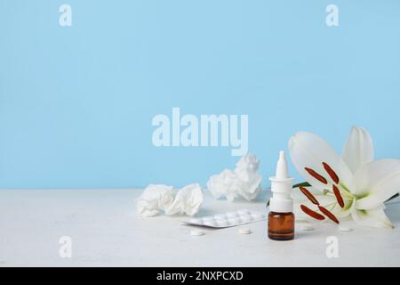 Nasentropfen mit Pillen, Blüten und Taschentüchern auf dem Tisch nahe der blauen Wand. Saisonales Allergiekonzept Stockfoto