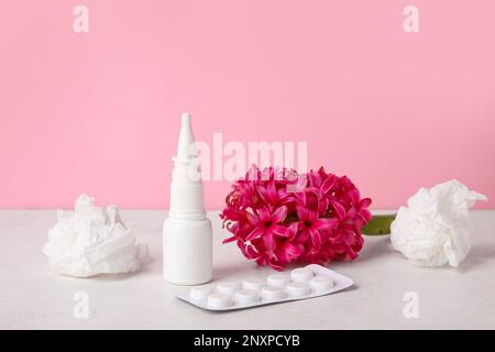 Nasentropfen mit Pillen, Blüten und Taschentüchern auf dem Tisch nahe der rosa Wand. Saisonales Allergiekonzept Stockfoto