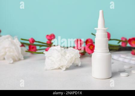 Nasentropfen mit Pillen, Blumen und Taschentüchern auf dem Tisch nahe der blauen Wand. Saisonales Allergiekonzept Stockfoto