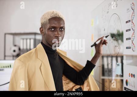 Selbstbewusster junger afrikanischer Mann in formeller Kleidung, der während eines Geschäftstreffens im Bürozimmer mit Papieraufklebern an Bord schreibt. Arbeitskonferenz- und Personenkonzept. Stockfoto