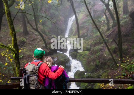 Ein Mann und eine Frau machen beim Wandern eine Pause, um einen Wasserfall auf dem Cataract Falls Trail in der Golden Gate National Recreation Area, Kalifornien, zu bewundern. Stockfoto