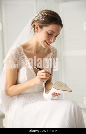 Die junge Braut schreibt die Namen ihrer Single-Freunde auf Schuhe. Hochzeitsabergläubisch Stockfoto