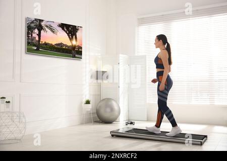 Sportliche Frau, die auf einem Laufband trainiert und zu Hause fernsieht Stockfoto