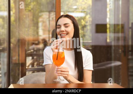 Junge Frau trinkt Aperol Spritz Cocktail in einem Café im Freien Stockfoto