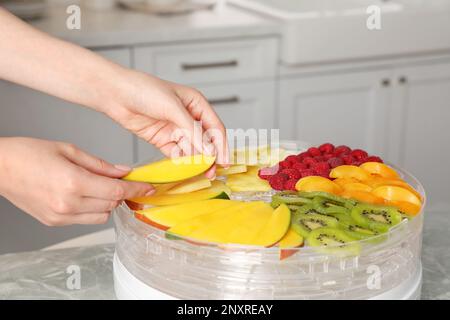 Eine Frau, die geschnittene Mango in die Fruchtentwässerungsmaschine in der Küche steckt Stockfoto