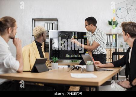 Fokussierter afrikaner spricht am Telefon, während seine männlichen Kollegen die Rede eines afroamerikanischen Geschäftsmanns hören. Firmenmanager, die im Büro arbeiten. Terminkonzept. Stockfoto