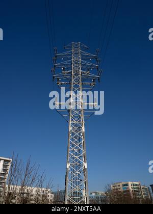 Ein Hochspannungspylon vor einem blauen Himmel und die Gebäude des Stadtviertels sind darunter zu sehen. Stockfoto