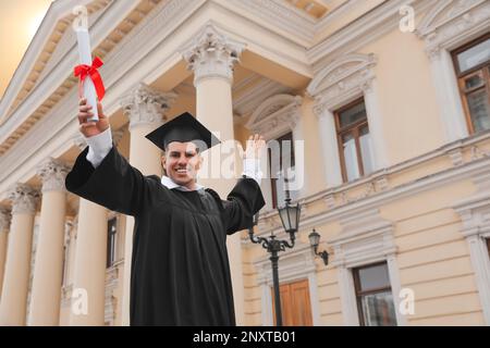 Glücklicher Student mit Abschluss nach der Abschlussfeier im Freien, Blick aus dem niedrigen Winkel. Platz für Text Stockfoto
