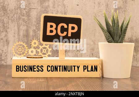 Auf einem hellen Bürotisch befinden sich ein Computer, ein schwarzer Taschenrechner, ein Stift und ein Notizbuch mit dem Text BCP Business Continuity Plan Stockfoto