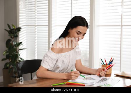 Eine junge Frau, die eine Anti-Stress-Seite am Tisch drinnen ausmalen kann Stockfoto