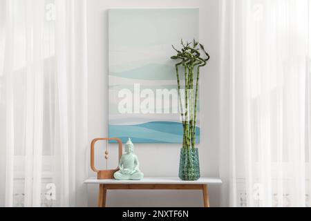 Konsolentisch mit Bambus- und Buddha-Statue in der Nähe von hellen Wänden im Innenbereich. Innendesign Stockfoto