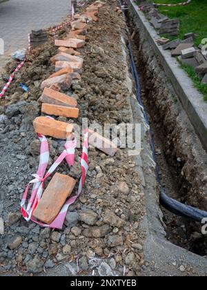 Kaputter Gehweg. Leitung des Kabels unter Tage. Kabelverlegungsarbeiten. Kommunikation in der Stadt. Elektrifizierung. Einen Graben nach Drähten graben. Stockfoto