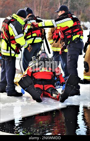 Feuerwehrleute mit dem Tauchteam der Feuerwehr üben ein Eisrettungsszenario am 11. Januar 2023 an einem gefrorenen Big Sandy Lake auf der South Post in Fort McCoy, Wisconsin. Mehrere Feuerwehrleute aus dem Team zogen einen Anzug an, schnallten sich einen Lufttank und eine Vollmaske an und tauchten in die Tiefen des Big Sandy Lake unter dem Eis an der South Post von Fort McCoy. Die Taucher bearbeiteten Tiefen von bis zu 15 Fuß oder mehr, um verschiedene Arten von Rettungsszenarien unter der Anleitung von anderen Feuerwehrleuten durchzuführen. Taucher wechselten sich ab und gingen in und aus dem gleichen Loch, das ich geschnitten hatte Stockfoto