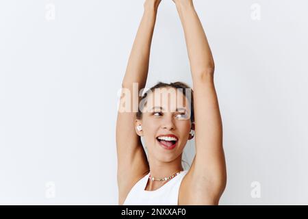 Eine Frau mit gebräunter Haut, die Musik hört und mit den Händen in den kabellosen Kopfhörern tanzt und mit ihren Zähnen vor einem weißen Gesicht lächelt Stockfoto