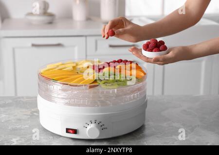 Eine Frau, die Himbeere in die Frucht-Entwässerungsmaschine am grauen Marmortisch in der Küche, Schließung Stockfoto