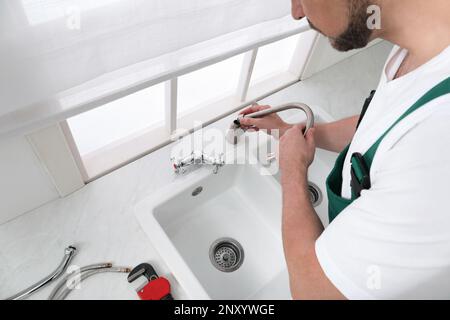 Professioneller Klempner, der den Wasserhahn in der Küche repariert, über der Aussicht Stockfoto