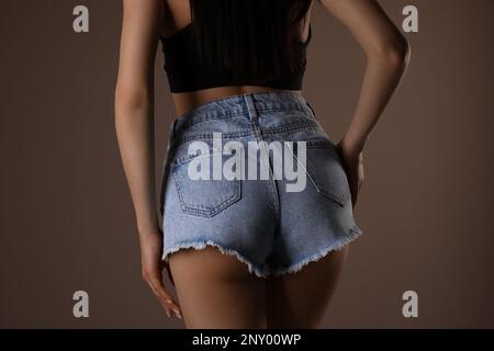 Schlanke Frau mit glatter Haut in Denim-Shorts auf beigem Hintergrund, Nahaufnahme. Cellulitenproblem-Konzept Stockfoto