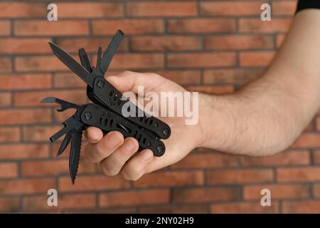 Ein Mann hält ein Multitool nahe einer Ziegelwand, Nahaufnahme Stockfoto