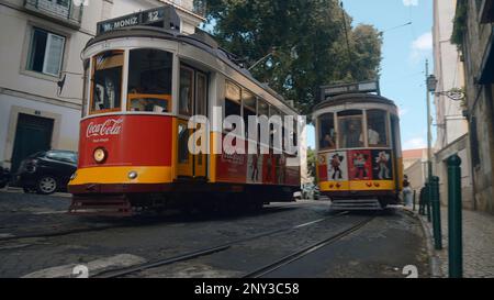 Portugal, Lissabon - 17. Juli 2022: Straßenbahnen, die durch die engen Gassen der europäischen Stadt fahren. Aktion. Straßenbahnen, die durch die europäischen Straßen der Altstadt fahren. Stockfoto