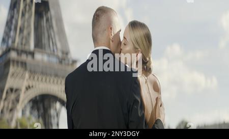 Ein europäisches Paar, das sich küsst. Aktion. Eine junge, wunderschöne blonde Frau mit ihrem Mann, der sich auf dem Eiffelturm küsst. Hochwertige 4K-Aufnahmen Stockfoto