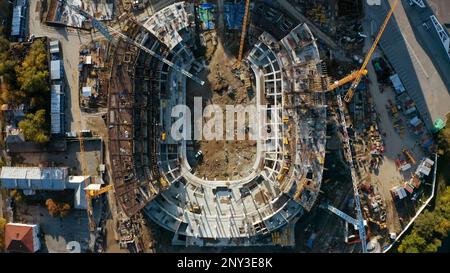 Draufsicht über den Stadionbau in der Stadt. Aktie-Aufnahmen. Bau eines modernen Sportstadions. Krane auf der Baustelle mit ovalem Stadion. Stockfoto