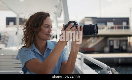 Schöne Frau, die Fotos auf dem Schiff macht. Aktion. Ein junger Fotograf mit lockigem Haar bläst auf die Gesichter, setzt sich hin und macht ein Foto von einem wunderbaren Su Stockfoto