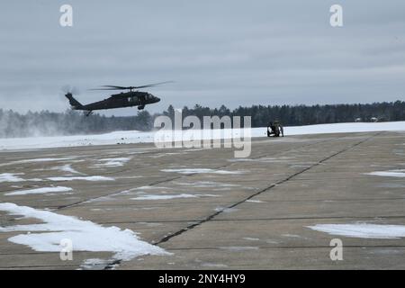 Ein Team von Soldaten des 1-120. Field Artillery Regiment, Wisconsin National Guard, bereitet sich darauf vor, einen M119 Howitzer an einen UH-60 Blackhawk vom 1-147. Aviation Regiment, Michigan National Guard, anzuhängen, während er während des Northern Strike 23-1, 23. Januar 2023, am Grayling Army Airfield, Michigan, eine Last mit einer Schlinge transportiert. Die Winterdurchführung von Northern Strike ist eine kostengünstige Möglichkeit für Einheiten des Verteidigungsministeriums, gemeinsame Operationen mit allen Bereichen bei kaltem Wetter durchzuführen. Stockfoto