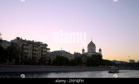 Abendlicher Blick auf die Stadt vom Fluss. Action. Ein Fluss, an dem Touristen auf Booten und einer großen weißen Kirche mit goldenen Kuppeln und der nahegelegenen Stadt mitgenommen werden Stockfoto