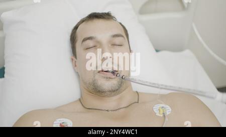 Im Operationssaal. Aktion. Ein Mann, der in einem Krankenhaus liegt, der sich ein Röntgenbild eines Herzschlags ansieht und der durch eine spezielle Röhre atmet. Hoch Stockfoto