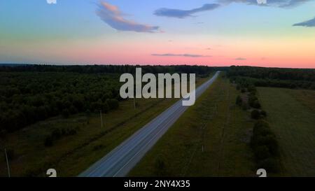 Blick von oben auf einen farbenfrohen, malerischen Himmel mit einer Straße. Clip.Landschaft, in der Sie die Straße mit Autos und großen grünen Feldern sehen können. 4K von hoher Qualität Stockfoto