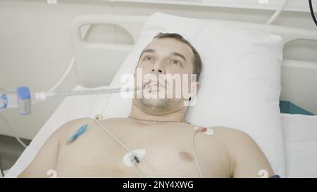 Im Operationssaal. Aktion. Ein Mann, der in einem Krankenhaus liegt, der sich ein Röntgenbild eines Herzschlags ansieht und der durch eine spezielle Röhre atmet. Hoch Stockfoto