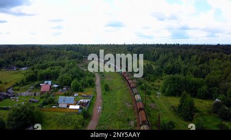 Eisenbahn aus der Höhe genommen. Clip. Eisenbahnen mit Güterzügen, die außerhalb der Stadt neben grünen Wäldern verkehren. Hochwertige 4K-Aufnahmen Stockfoto