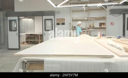 Weibliche Mitarbeiterin im Fabriklager mit Brettern. Kreativ. Arbeiter im Anzug schickt Tafeln zum Malen. Die Frau in der Firma malt Holz Stockfoto