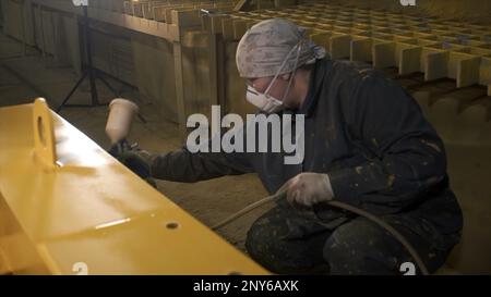 Arbeiter lackiert Stahlteile mit einer Spritzpistole. Clip. Weibliche Mitarbeiterin lackiert Stahlteile in der Fabrik. Spritzlackierung von Industrieteilen. Stockfoto