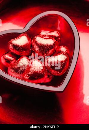 Kleine rote Schokoladenherzen in einer herzförmigen Glasschüssel Stockfoto