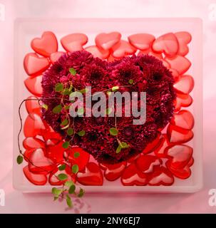 Herz aus Blumen mit roten Glasherzen Stockfoto