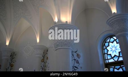 Ein helles weißes Gebäude mit gedämpfter Beleuchtung. Szene. Riesige, weiß dekorierte Säulen mit sanfter orangefarbener Beleuchtung. Hochwertige FullHD-Aufnahmen Stockfoto