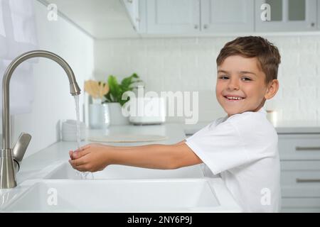 Ein Junge, der Hände unter Wasser hält und in der Küche aus dem Wasserhahn läuft Stockfoto