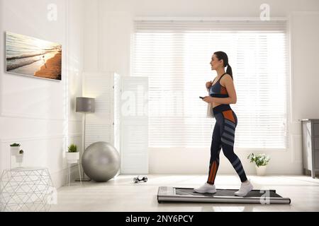 Sportliche Frau mit Fernbedienungstraining auf Laufband und Fernsehen zu Hause Stockfoto