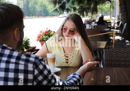 Junge Frau hat ein langweiliges Date mit einem Typen im Café draußen Stockfoto