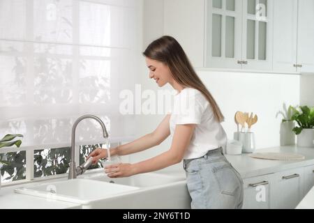 Frau, die Glas mit Wasser aus dem Wasserhahn in der Küche füllt Stockfoto