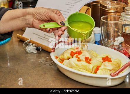 Der Koch gießt Sauce auf Kohlbrötchen mit Lachs und Karotten in der Küche. Französisches Rezept. Stockfoto