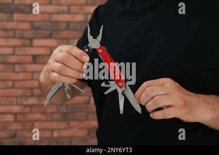 Ein Mann hält ein Multitool nahe einer Ziegelwand, Nahaufnahme Stockfoto