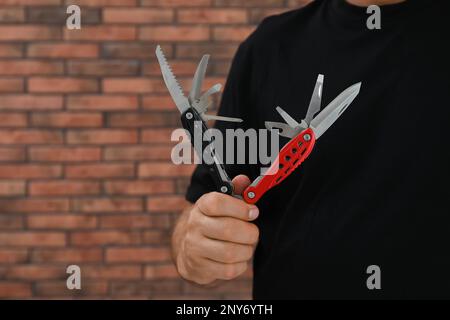 Ein Mann hält ein Multitool nahe einer Ziegelwand, Nahaufnahme. Platz für Text Stockfoto