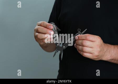 Ein Mann hält ein Multitool auf grauem Hintergrund, Nahaufnahme Stockfoto