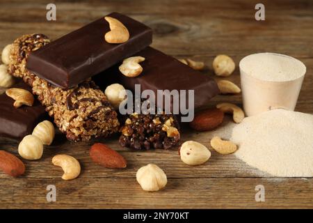 Verschiedene leckere Riegel, Nüsse und Eiweißpulver auf Holztisch Stockfoto