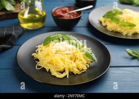 Leckerer Spaghetti-Kürbis mit Basilikum und Käse auf einem blauen Holztisch Stockfoto