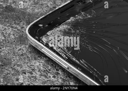 Smartphone mit rissigem Bildschirm auf grauem Steinhintergrund, Nahaufnahme. Gerätereparatur Stockfoto