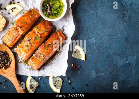 Köstliches gebratenes Lachsfilet, Gewürze auf blauem rustikalem Betonhintergrund. Gekochtes Lachssteak mit Pfeffer, Kräutern, Zitrone, Knoblauch, Olivenöl Stockfoto